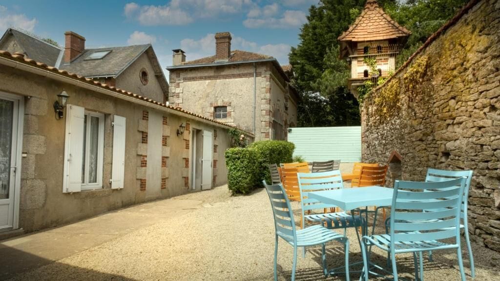 A courtyard with a table and chairs, stone walls, and a small tower-like structure.