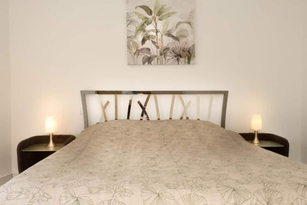 Une chambre à coucher avec un lit, deux tables de chevet et un tableau accroché au mur.