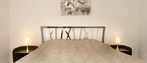 A bedroom with a bed, two bedside tables, and a wall-mounted painting.