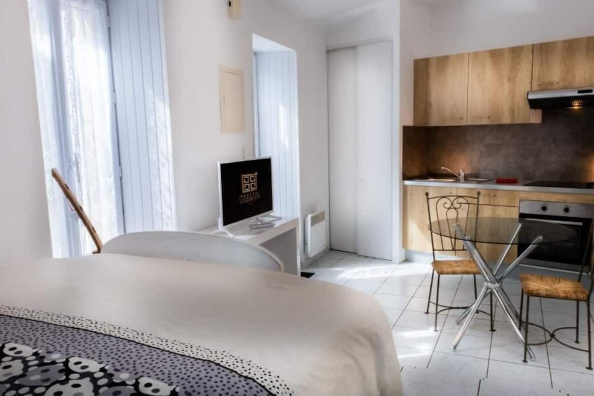 Une chambre d’hôtel moderne équipée d’un lit, d’un bureau avec un ordinateur, d’une table à manger avec des chaises et d’un coin cuisine.