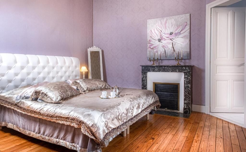 Een slaapkamer met een gebonden hoofdbord, een open haard en een groot bloemen schilderij aan de muur.
