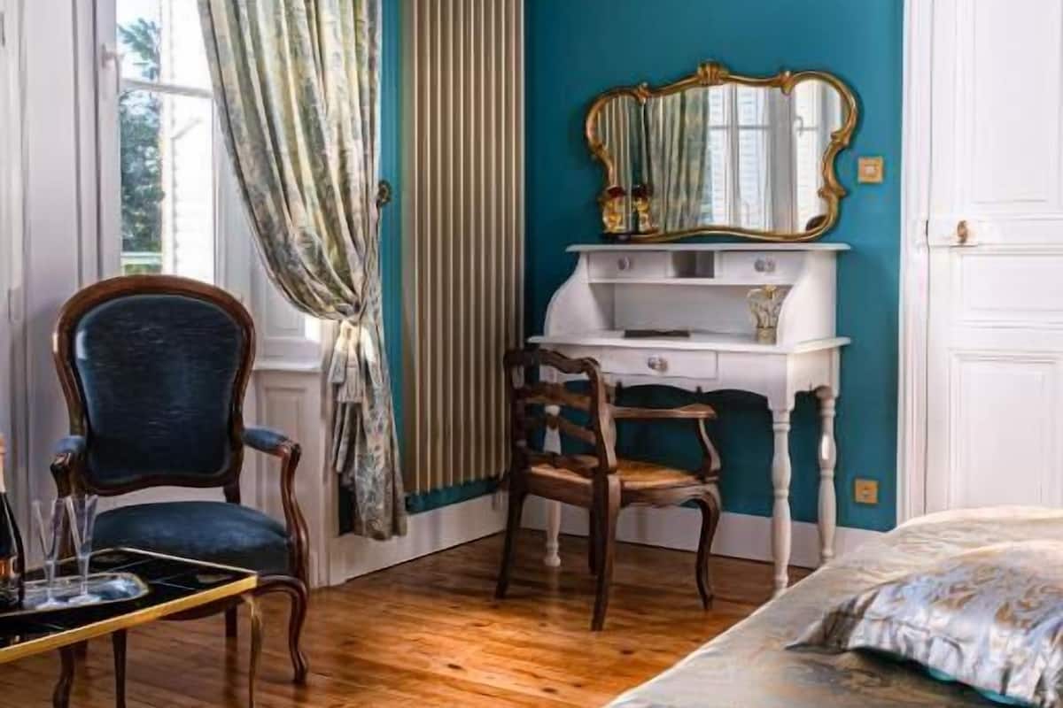 Une pièce comprenant un lit, un bureau, une chaise et une fenêtre avec des rideaux.