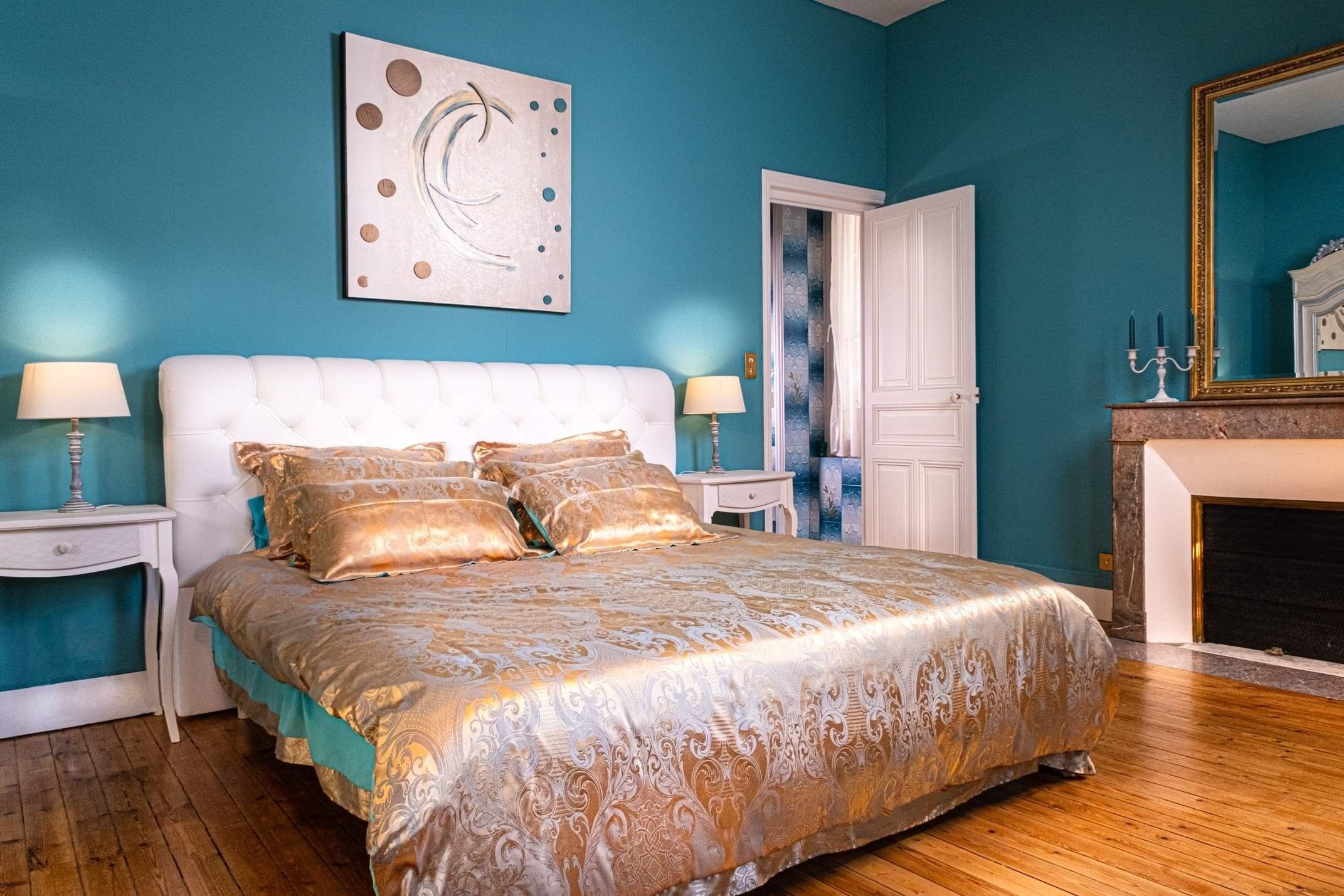 A bedroom with a large bed, two bedside tables, a wall-mounted artwork, a door, and a fireplace.