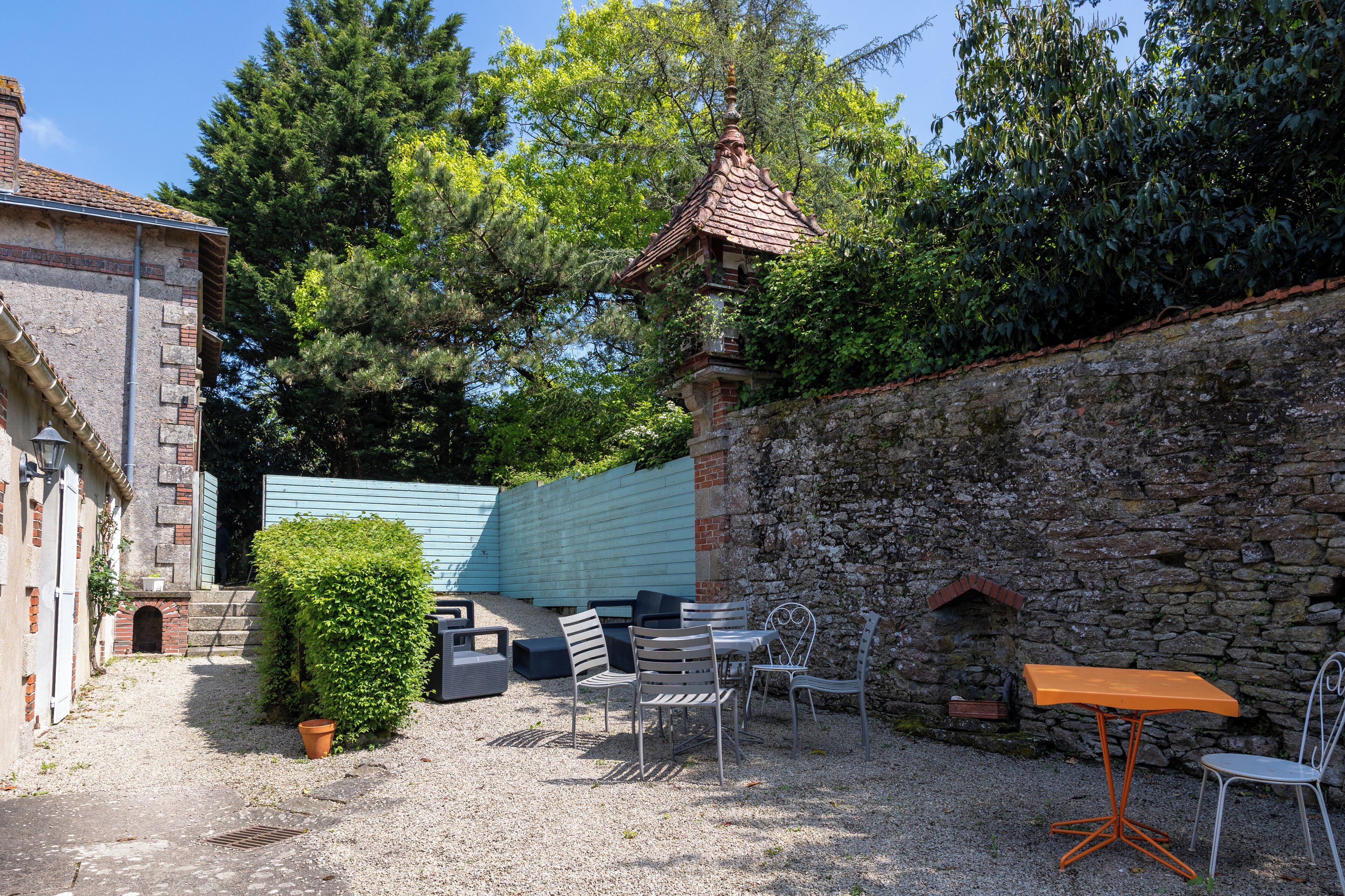 An outdoor seating area with stone walls, a small brick structure, and a metal table and chairs.