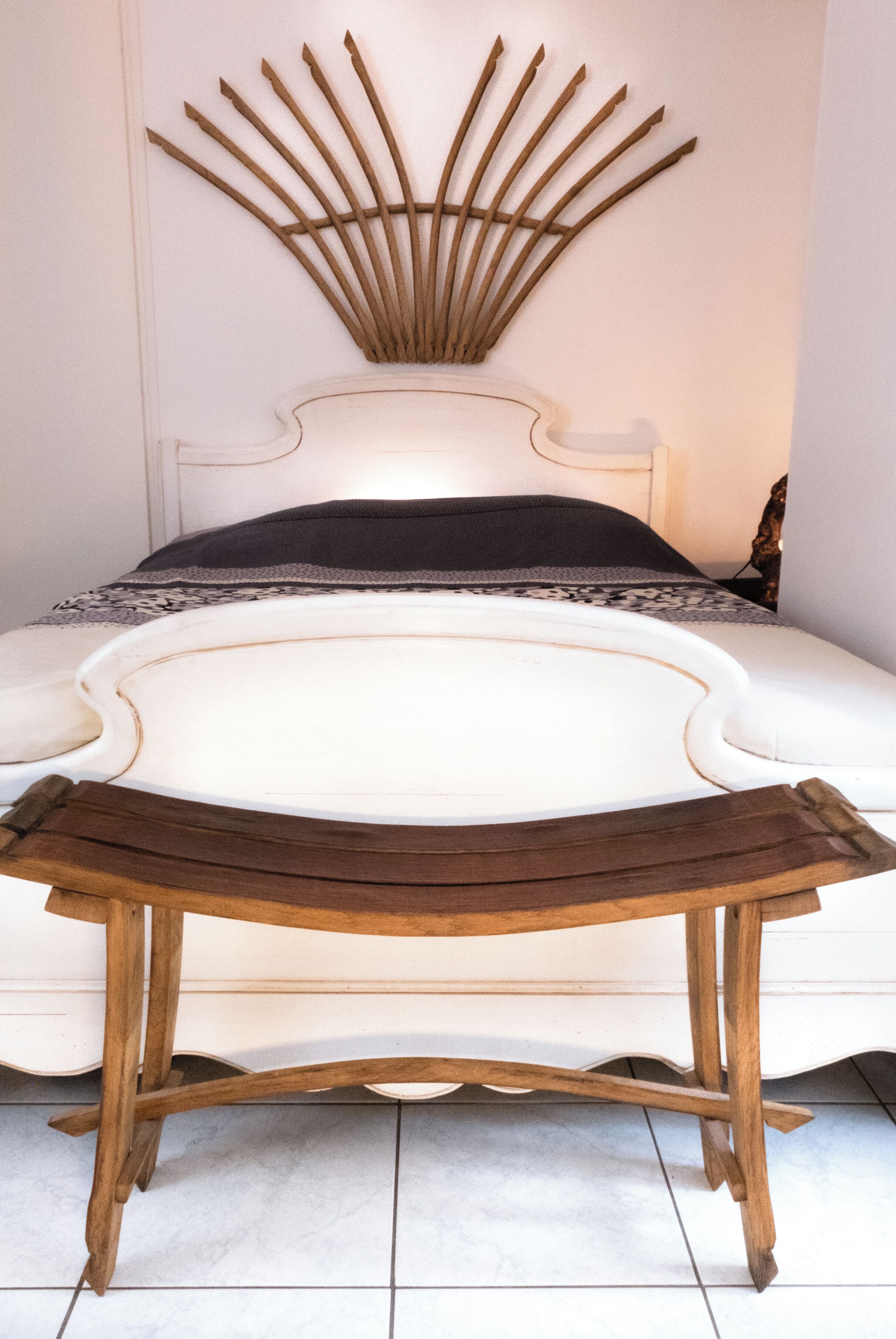A bed with a white headboard, a wooden bedside table, and a decorative wall piece above the bed.