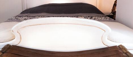 A bed with a white headboard, a wooden bedside table, and a decorative wall piece above the bed.