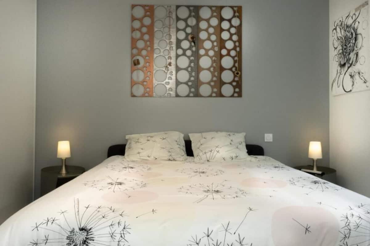 Une chambre avec un grand lit, deux tables de chevet avec des lampes et une œuvre d’art murale au-dessus du lit.