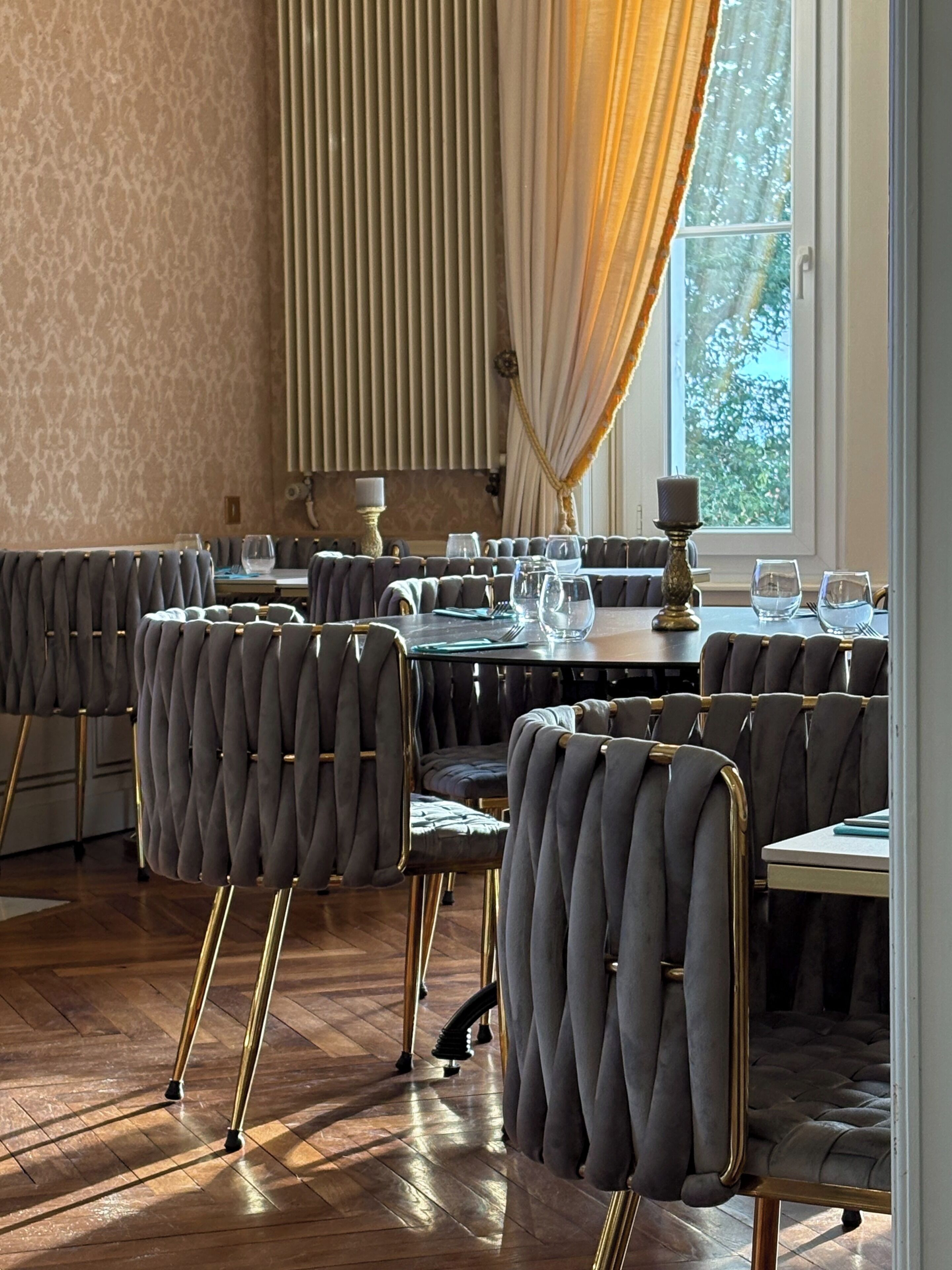Un comedor con sillas tapizadas grises, una mesa redonda y una ventana con cortinas.
