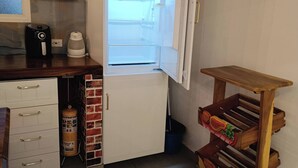 Cocina compacta con refrigerador, cafetera y frutero sobre un pedestal de madera.