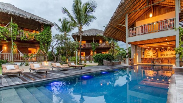 A resort with a swimming pool, lounge chairs, and thatched-roof buildings.