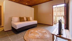 A room with a wooden ceiling, a sofa with cushions, a woven rug, and a television on a wooden stand.
