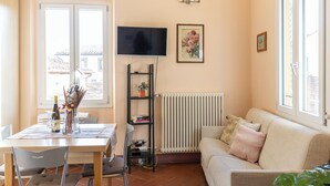 A living room with a sofa, a TV mounted on the wall, a bookshelf, and a dining area with chairs and a table. - Strozzi Apartment with view (Firenze)