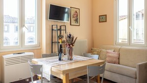 A living room with a sofa, a TV mounted on the wall, a dining table with chairs, and a radiator. - Strozzi Apartment with view (Firenze)