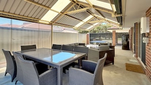 Ein überdachter Patio-Bereich mit Tischplatte aus Glas, Korbstühlen, einem Grill und einer Ziegelwand.