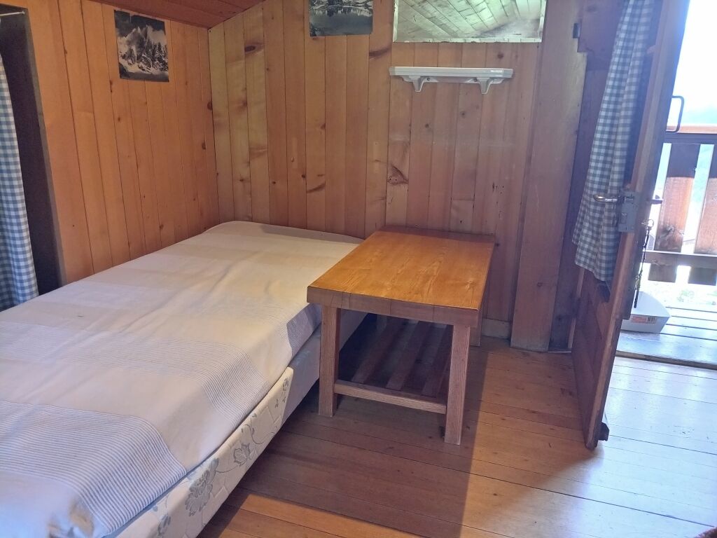 A wooden room with a bed, a small wooden table, and a window with a view.