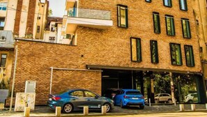 Un edificio de varios pisos con fachada de ladrillo, múltiples ventanas y un estacionamiento con coches.