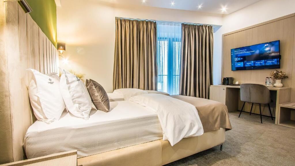 A modern hotel room with a large bed, a desk, a chair, and a flat-screen TV.