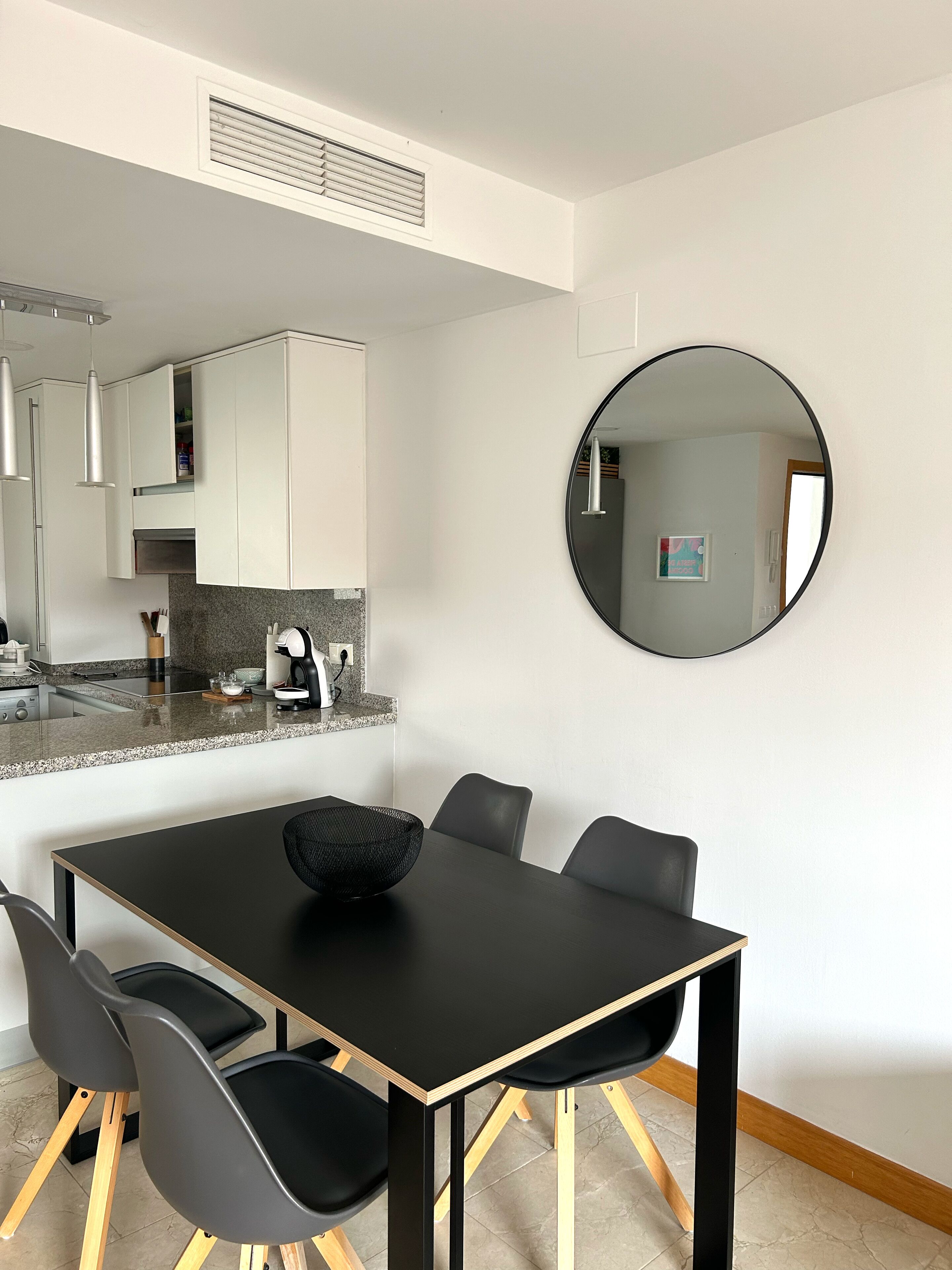 A modern kitchen with white cabinets, a granite countertop, and a black dining table with four chairs.