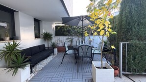 En moderne udendørs terrasse med en sort sofa, stribede stole og en potteplante.