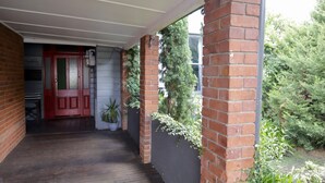A covered porch with a wooden floor, brick walls, and a red door. - Towncottage Tenterfield Stay With Scenic Views (Tenterfield)