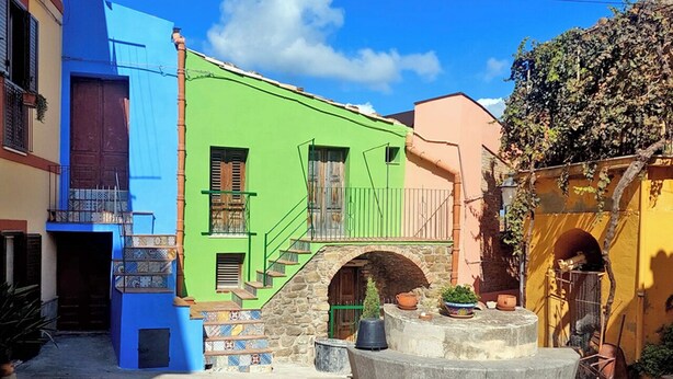 Un patio con edificios de colores, una escalera de piedra y una fuente central.
