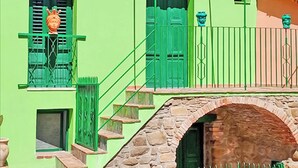 Un edificio con un arco de piedra, contraventanas verdes y una escalera que lleva a un balcón.