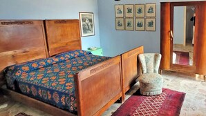 Un dormitorio con una cama de madera, una silla, un tapete estampado en rojo y cuadros enmarcados en la pared.