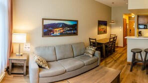 Un salon comprenant un canapé, une table à manger et des chaises. Un tableau représentant un paysage de montagne est accroché au mur.