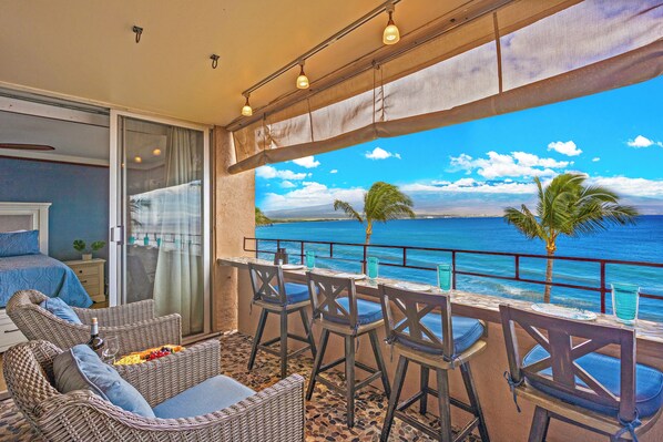 A balcony with wicker furniture, a table with chairs, and a view of the ocean. - Where Ocean Meets Sky Maalaea Refreshed Oceanfront Condo Panoramic Views (Wailuku)