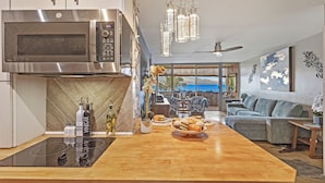 Una cucina moderna con forno a microonde integrato, un'isola in legno con piano in vetro e un'area salotto con vista sull'oceano.