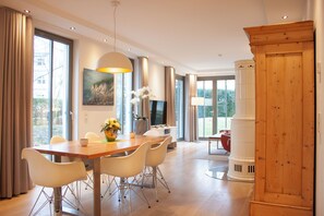A spacious dining area with a wooden table and white chairs, a large window with curtains, a painting on the wall, and a wooden cabinet. - Luxury vacation apartment Seestern with private beach chair & pool | terrace | Binz (Binz)