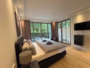 Une chambre moderne avec un grand lit, un téléviseur à écran plat et une vue sur la verdure par les fenêtres.