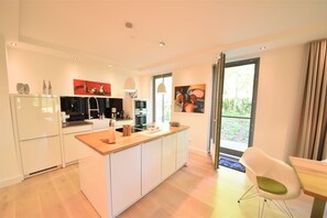 A modern kitchen with white cabinetry, a wooden countertop, and a dining area with a white chair. - Seestern Vacation Rental with Beach Chair & Pool | Terrace | Family (Binz)