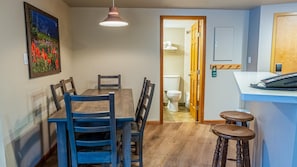 A dining area with a wooden table and chairs, a hanging pendant light, and a painting on the wall. - Cahilty #249 2 Bedroom Hotel Room (Sun Peaks)