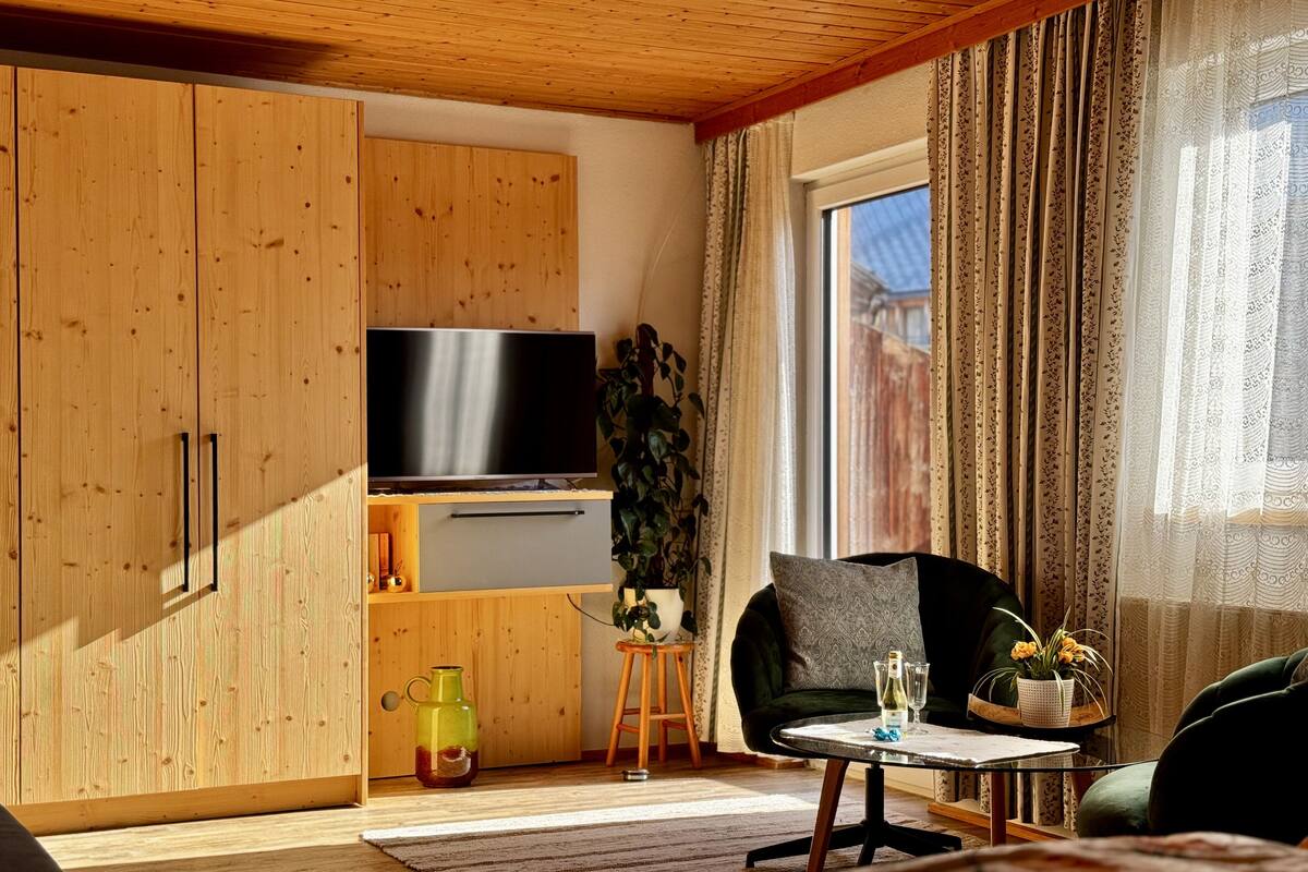 A modern living room with wooden cabinets, a flat-screen TV, a sofa, a coffee table, and a large window with curtains.