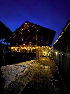 A two-story wooden house with a snow-covered driveway and festive lights. - Heli's Holiday Suites (Altaussee)