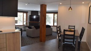 A modern living room with a fireplace, a dining area with a table and chairs, and a kitchen with wooden cabinets.