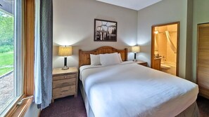 Habitación de hotel con cama, dos mesitas de noche con lámparas, cabecero, un cuadro enmarcado en la pared y una ventana con cortinas.