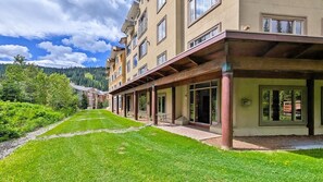 Un hotel con un área exterior techada, un césped y montañas al fondo.