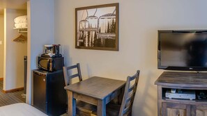 A hotel room with a bed, a desk with a chair, a coffee maker, a microwave, a TV, and a framed picture on the wall. - Cahilty #234/236 1 Bedroom Hotel Room (Sun Peaks)
