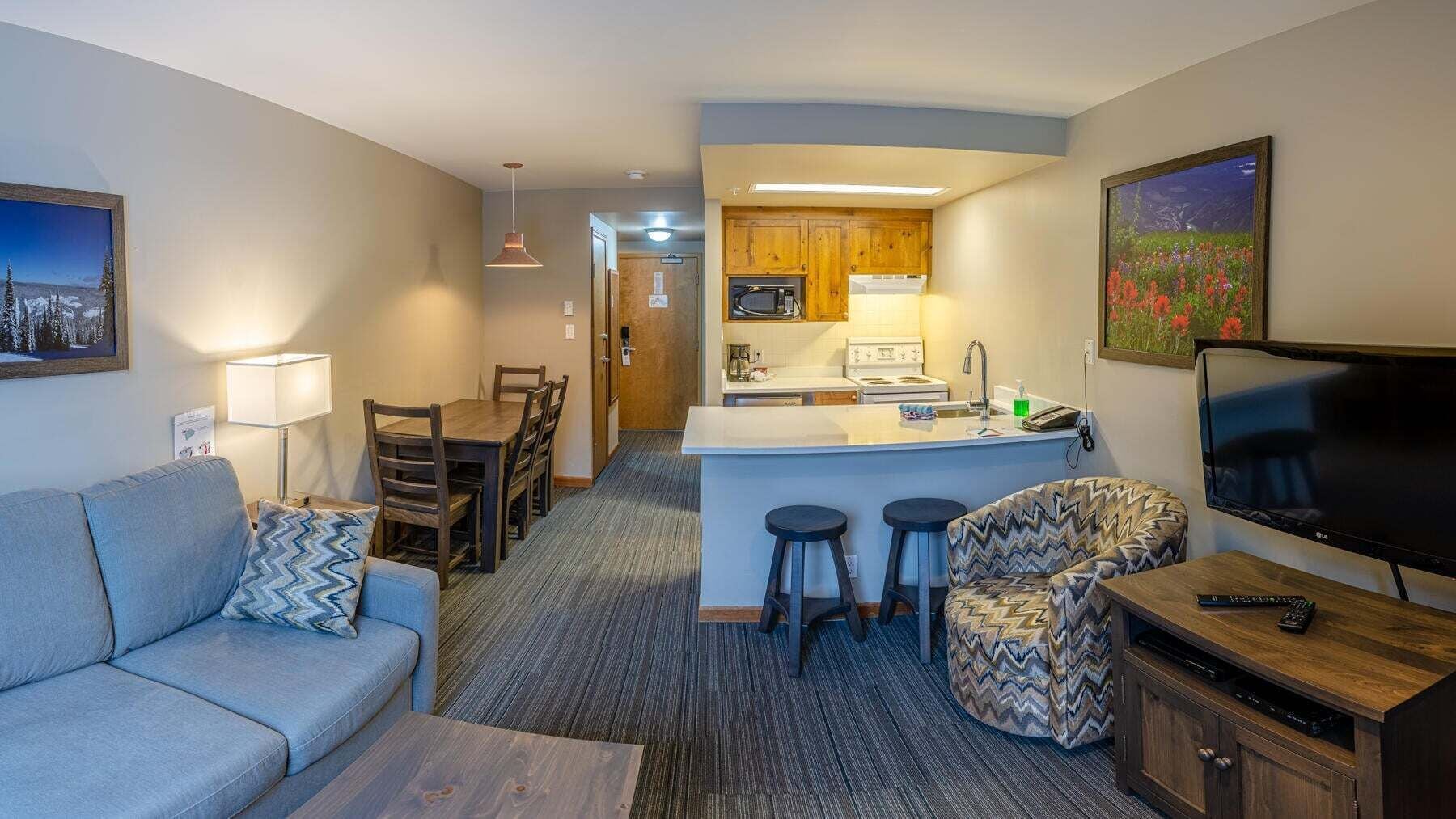 A compact living space with a kitchenette, a dining area, a sofa, a TV, and a bar area.