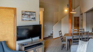 A living room with a flat-screen TV, wooden entertainment unit, and a dining area with a table and chairs.