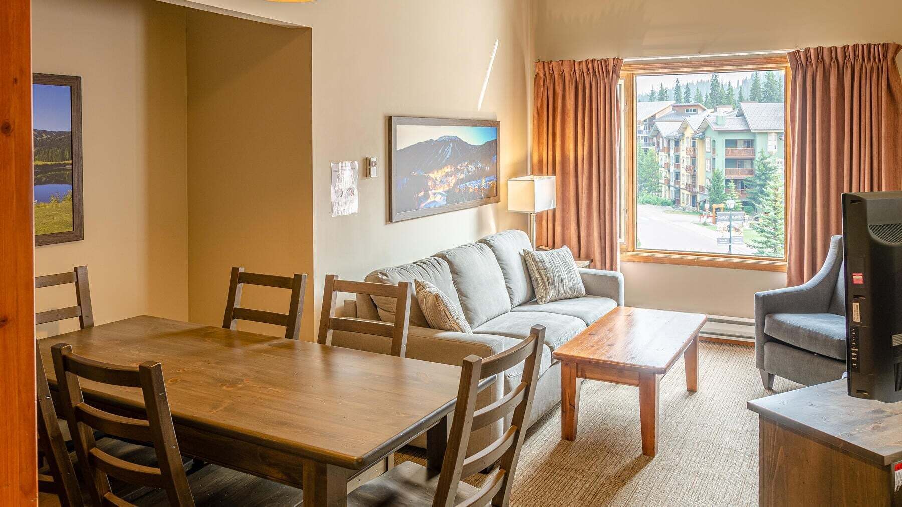 A cozy hotel room with a dining table, sofa, and a TV on a wooden stand.