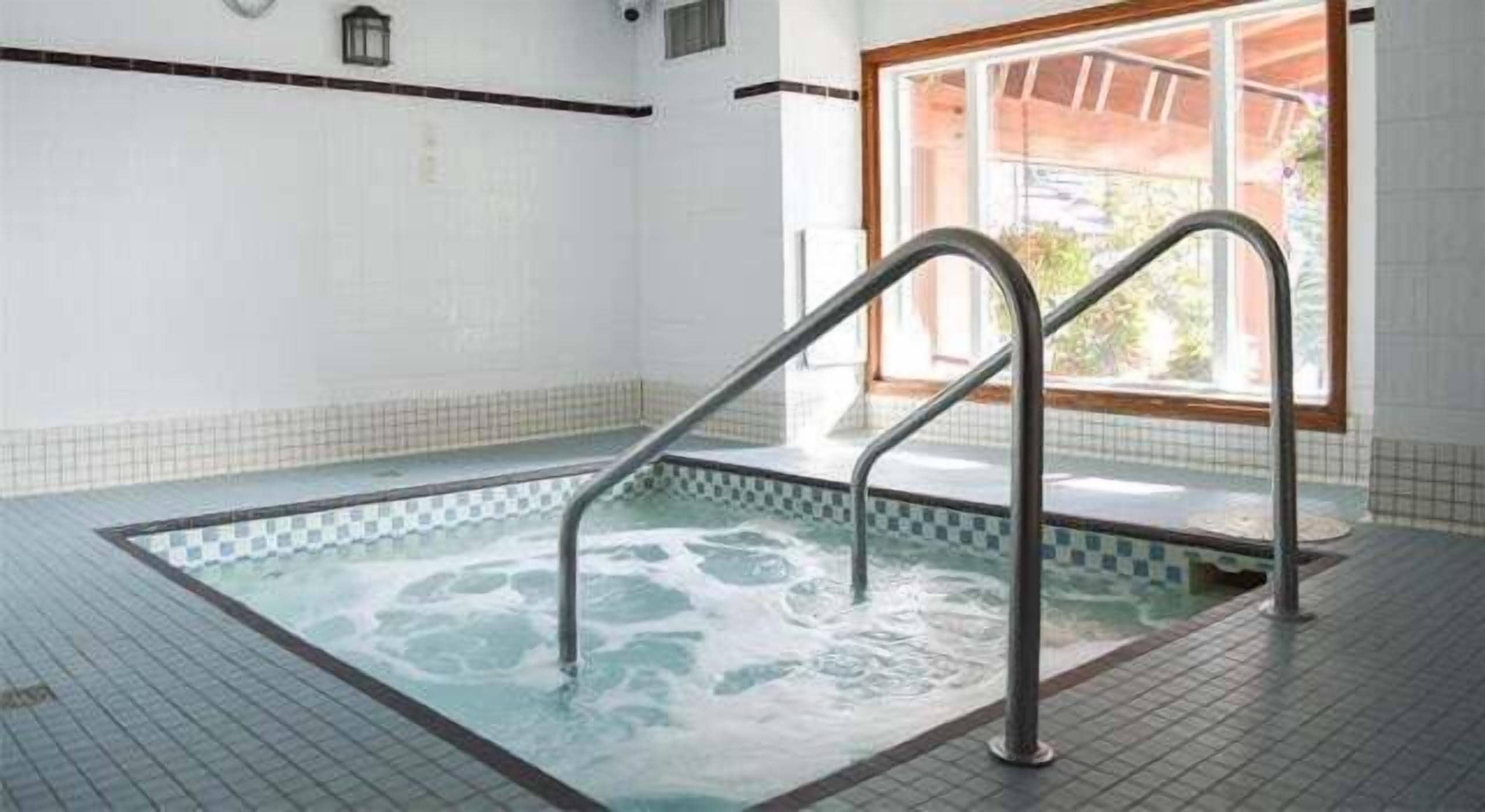 An indoor swimming pool with clear water, metal ladders, and a tiled floor.