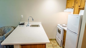 Cocina compacta con encimera blanca, un fregadero, estufa y refrigerador.