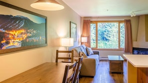 A cozy living room with a wooden dining table, a sofa, and a large window with curtains.
