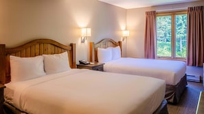 A hotel room with two beds, wooden headboards, bedside lamps, a telephone, and a window with curtains.