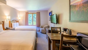 Habitación de hotel con dos camas, un escritorio con silla, un televisor y un cuadro en la pared.