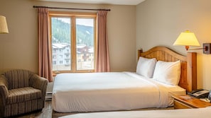 A hotel room with a bed, a chair, a nightstand, and a window with curtains. - Cahilty #334/336 1 Bedroom Hotel Room (Sun Peaks)