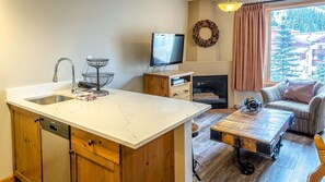 A compact kitchen with a sink, wooden cabinets, and a dining area with a table and sofa. - Cahilty #334/336 1 Bedroom Hotel Room (Sun Peaks)